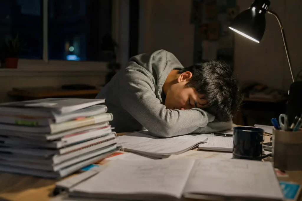 student śpiący przy biurku obok stosu notatek